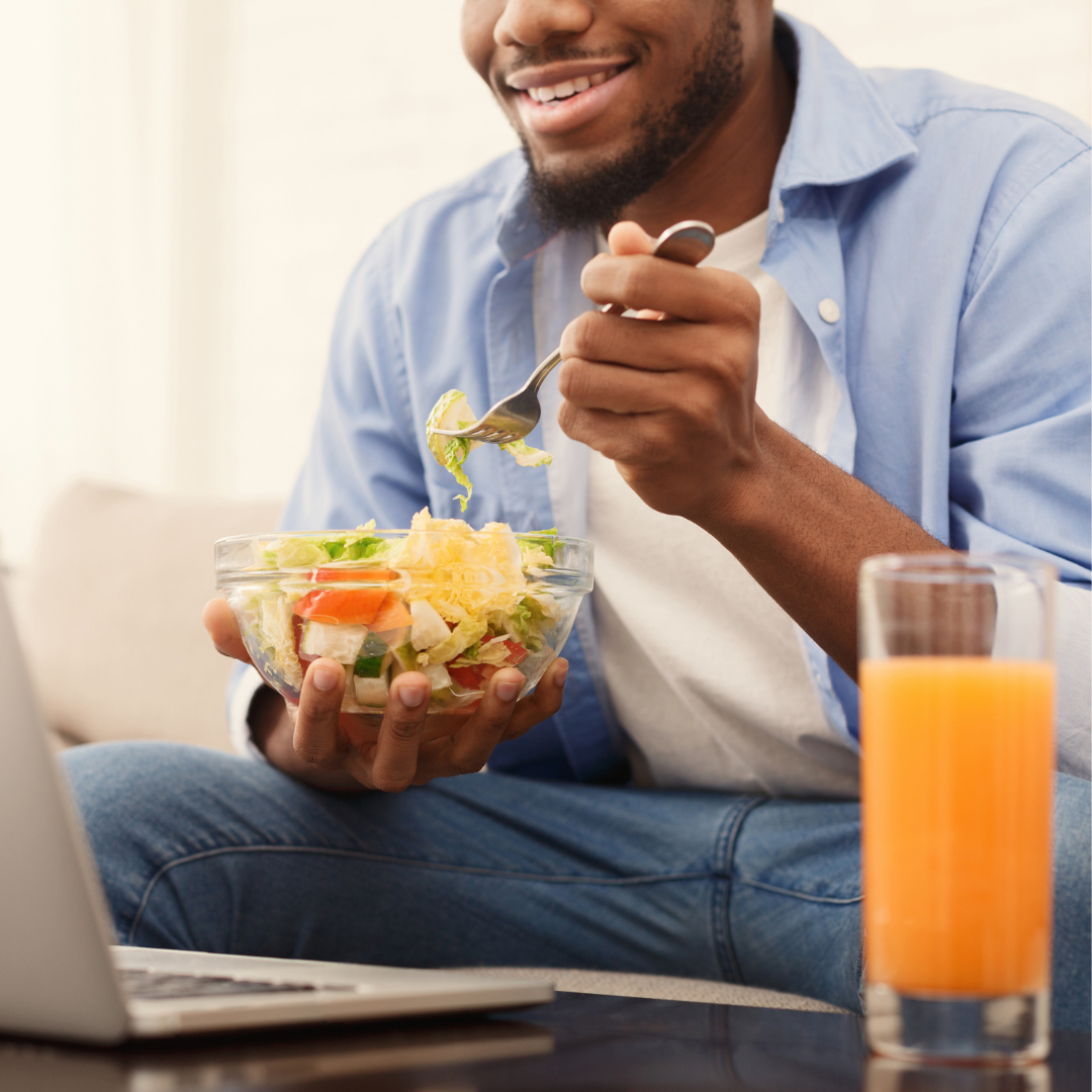 man sits at computer eating salad
